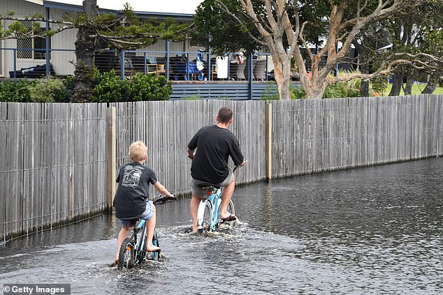Two boys ride their bikes through continued floodwater from Lake Ainsworth across the main road on April 15, 2022 in Lennox Head, Australia